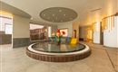 A modern reception area with a round water basin in the center. In the middle stands a colorful figure with a red hat and a yellow lounge chair.
