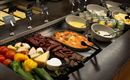 A rich buffet with various types of meat, cheese, fresh vegetables, and dips. Next to it, there are several bowls of desserts and a creamy sauce.