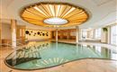 An elegant indoor pool with modern design and warm wooden elements. Natural light streams through the skylight, creating a relaxing atmosphere.