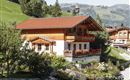 A charming chalet in the Alps with a red roof and blooming flowers. Surrounded by green meadows and wooded mountains.