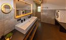 A modern bathroom with a large sink and a mirror surrounded by soft light. On the right side, there is a washing machine.