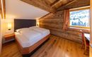 A cozy bedroom with a double bed and wooden walls. The room has a window overlooking nature and a small desk.