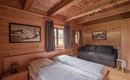 Ein gemütliches Schlafzimmer mit Holzwänden und zwei Einzelbetten. Es gibt einen Schlafsofa und große Fenster mit Vorhängen.
