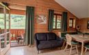 Ein gemütliches Zimmer in einem Holzhaus mit Blick auf die grüne Landschaft. Es gibt ein Sofa und einen Esstisch mit Stühlen.