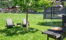 Ein ruhiger Garten mit zwei Liegestühlen, einem Grill und einem Trampolin. Im Hintergrund sind Häuser und grüne Berge zu sehen.