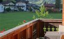 Ein schöner Balkon mit einem Tisch und Stühlen blickt auf eine malerische Landschaft. Im Hintergrund sind Berge und typische alpine Häuser zu sehen.
