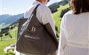 A person is carrying a large bag with the logo "Bergengut". In the background, green hills and a clear sky can be seen.