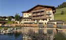 A modern hotel building in the midst of a green landscape. The clear pond reflects the surroundings.