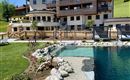 A modern hotel with large balconies and a pool. The surroundings are green and inviting, ideal for a relaxing stay.