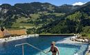 A pool in the mountains with a person stepping into it. Surrounded by green hills and blue sky.