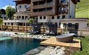 A modern hotel with an outdoor pool and a beautiful garden area. The surroundings are green and provide a tranquil atmosphere.