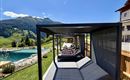 A quiet outdoor area with loungers and a pool. The surrounding landscape is green and mountainous under a clear blue sky.