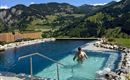 A beautiful pool in the mountains with clear water. In the background, green hills and a blue sky can be seen.