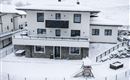 A modern house in the snow with a large balcony and a playground in the foreground. The surroundings are quiet and wintry.