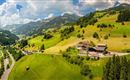 Eine wunderschöne grüne Landschaft mit sanften Hügeln und einem klaren Himmel. Man sieht ein paar Gebäude und eine kurvenreiche Straße in der Umgebung.