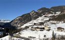 Eine malerische Winterlandschaft mit schneebedeckten Bergen und Hütten. Der klare blaue Himmel über dem ruhigen Tal vermittelt eine friedliche Atmosphäre.