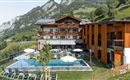 A modern hotel building is located amidst the mountains. In front of the hotel, there is a pool and a well-maintained garden landscape.