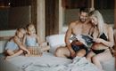 A family is relaxing in a modern room. The children are playing with a toy while the parents are reading a magazine.