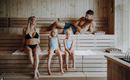 A family is relaxing in a sauna. Two girls and their parents are sitting on the wooden benches and enjoying their time together.