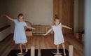 Two girls are standing on balance cushions and practicing their balance. They are wearing light blue dresses and look happy.