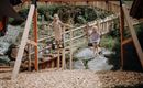Two children are playing in a playground. One child is swinging on a swing, while the other is walking on a balance beam.