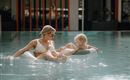 A mother and her child relax in a pool. They are happily playing in the water and enjoying the sun.