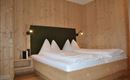 A modern bedroom with wood paneling and a large double bed. The walls are bright and friendly, with stylish wall lamps.