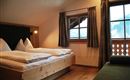 A cozy bedroom with wooden beds and large windows. The atmosphere is warm and inviting, ideal for a relaxing stay.