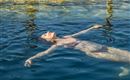 Eine Frau liegt entspannt im Wasser und genießt die Ruhe. Das Licht spiegelt sich sanft auf der Wasseroberfläche.