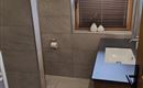A modern bathroom with tiles and a window. There is a hand wash basin and a privacy screen.