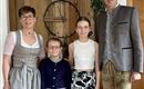 Eine Familie in traditioneller bayerischer Tracht steht in einem gemütlichen Raum. Sie lächeln freundlich und posieren für das Foto.