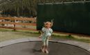 Ein Mädchen springt fröhlich auf einem Trampolin. Im Hintergrund sind Bäume und eine grüne Wand zu sehen.