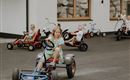 Eine Gruppe von Kindern fährt auf Pedal-Gokarts. Die Szenen spielen sich auf einem gepflasterten Bereich vor einem Gebäude ab.