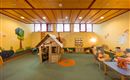 A cozy playroom with a wooden playhouse and colorful wall murals. There are comfortable armchairs and toys on the floor.