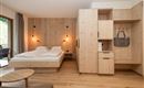 Ein modernes Zimmer mit Holzwänden und einem gemütlichen Doppelbett. Die Einrichtung ist schlicht und angenehm, mit einem Schrank und einem kleinen Tisch.