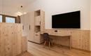 Ein modernes Arbeitszimmer mit einer Holzoptik. Es gibt einen Fernseher an der Wand und einen Schreibtisch mit einem Stuhl.
