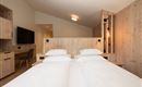Ein modernes Hotelzimmer mit zwei Betten und natürlichem Holzdekor. Der Raum ist hell und freundlich gestaltet, mit einem Fernseher und stilvollen Lampen.