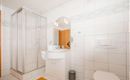 A modern bathroom with white tiles and a shower. There is a sink, a mirror, and a toilet.