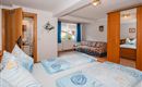 A cozy bedroom with two beds and colorful bedspreads. The room features a window with curtains and a couch.