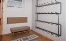 A hallway with a brown tiled floor and a wooden ceiling.  
On the wall, there is a shoe rack and a bench.