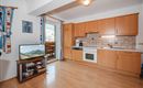 A modern kitchen with wooden cabinets and a light floor. In the room, there is a television and there is a view of the mountains through the window.