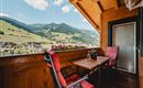 A cozy balcony with a view of green hills and mountains. The table and chairs invite you to relax.