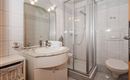 A modern bathroom with a glass shower and a sink. The walls are tiled and there is a large mirror.
