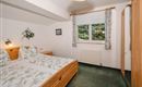 A cozy bedroom with two beds and green bedding. The windows offer a view of nature and the room is bright and pleasantly furnished.
