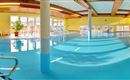 A bright indoor pool with clear water and a friendly yellow hue. There are lounges and windows that provide plenty of daylight.