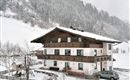 A charming house in the snow with traditional architecture. The surroundings are surrounded by snow-covered mountains and trees.