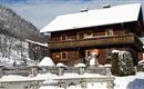 A beautiful wooden house in the snow with a balcony. The surroundings are wintry, surrounded by mountains and snow-covered trees.