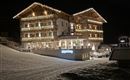 A cozy hotel, festively lit at night. It is surrounded by snow and radiates a warm atmosphere.