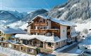 A cozy hotel in the snow with large windows and balconies. In the background, snow-covered mountains can be seen.