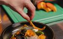 Ein kunstvoll angerichteter Teller mit Fisch, Gemüse und Kräutern. Im Hintergrund wird zusätzlich Obst vorbereitet.